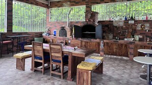 An outdoor kitchen area with a brick oven, wooden furniture, and a bar with various bottles.