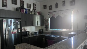 A kitchen with a stainless steel refrigerator, a microwave, a toaster, and a gas stove. There are cabinets above the counter and a window with a curtain.