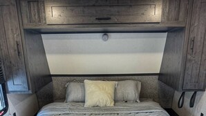 Un intérieur de camping-car compact et moderne, doté d’un lit, de placards de rangement et d’un coin salon intégré.
