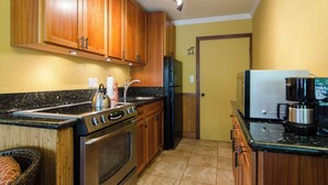 A kitchen with wooden cabinets, a stove, a refrigerator, and a coffee maker. - Cozy  studio condo with AC and WiFi in charming Koloa/ Poipu (Koloa)