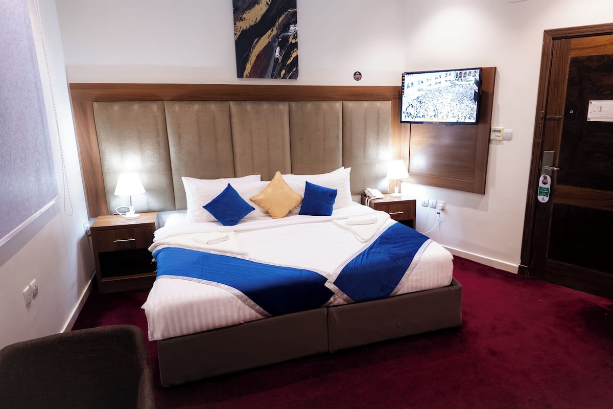 A hotel room with a large bed, a wooden headboard, a TV mounted on the wall, and a door with a security lock.