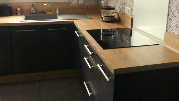 Una cucina moderna con mobili scuri, un piano di lavoro in legno e un piano cottura integrato.
