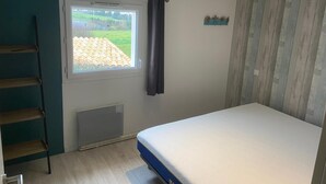 Une chambre à coucher avec un lit, une fenêtre avec des rideaux, un radiateur, une échelle en bois et un mur orné de panneaux de bois.