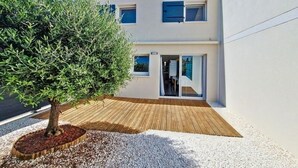 Un edificio moderno a due piani con una terrazza in legno e un albero sullo sfondo.