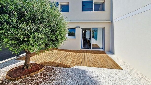 Un bâtiment moderne à deux étages, doté d’une terrasse en bois et d’un arbre en premier plan.