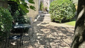 A patio area with a stone table and chairs, surrounded by greenery and a stone building.