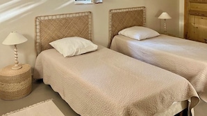 A room with two single beds, a wooden ceiling, a window, and a door.