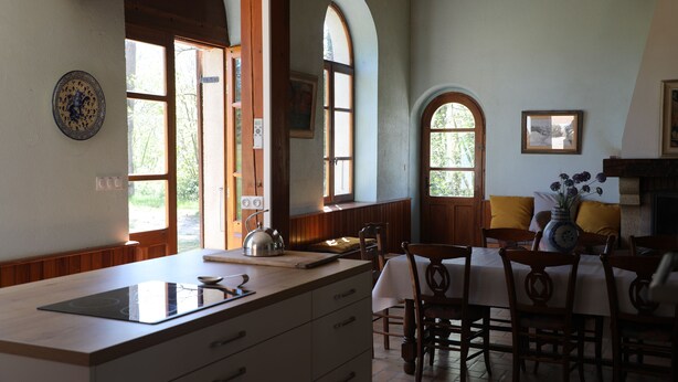 Una cocina con una isla central, armarios de madera y un comedor con mesa y sillas.