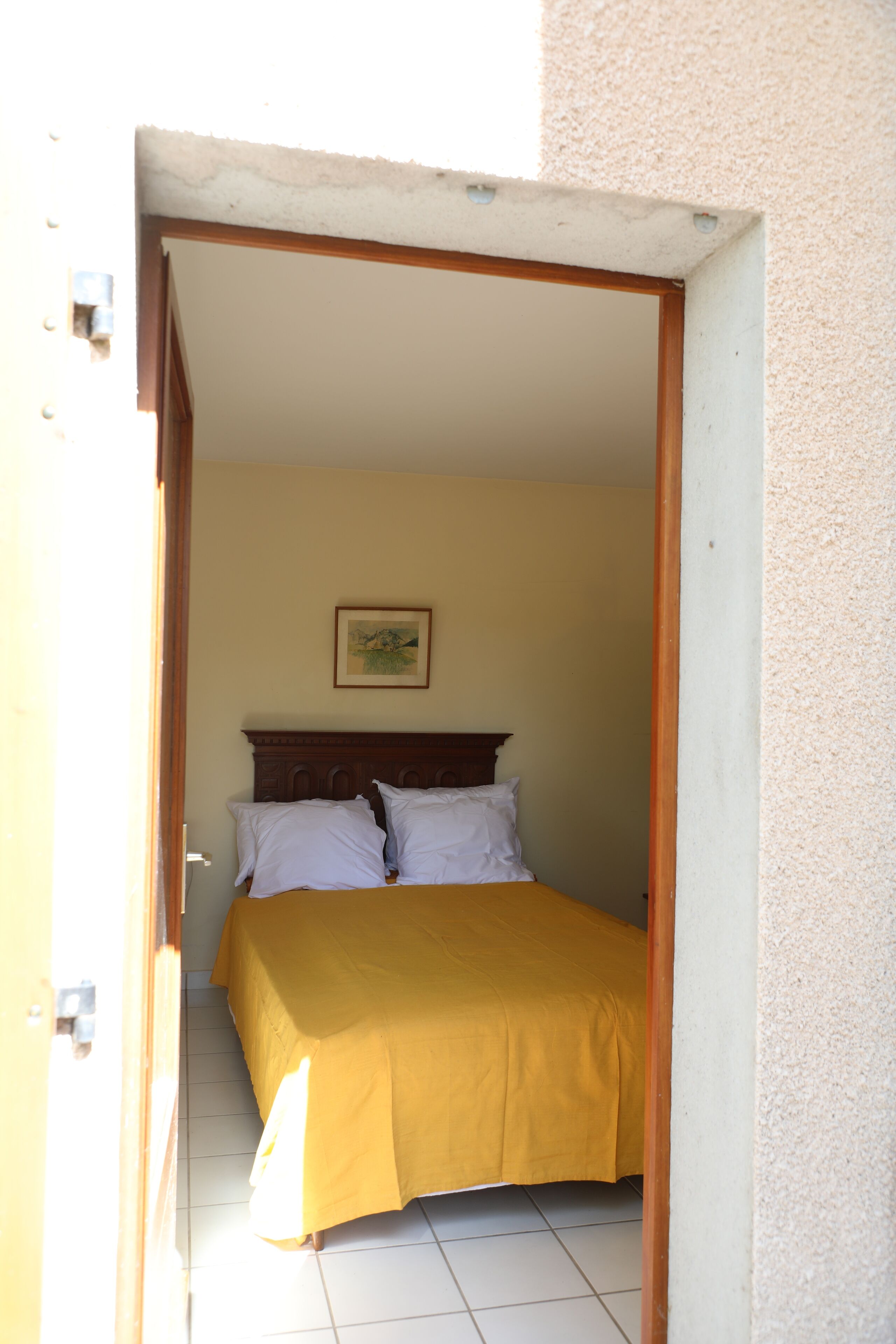 Une chambre à coucher avec un lit, une tête de lit en bois, une couvre-lit jaune et un tableau encadré accroché au mur.