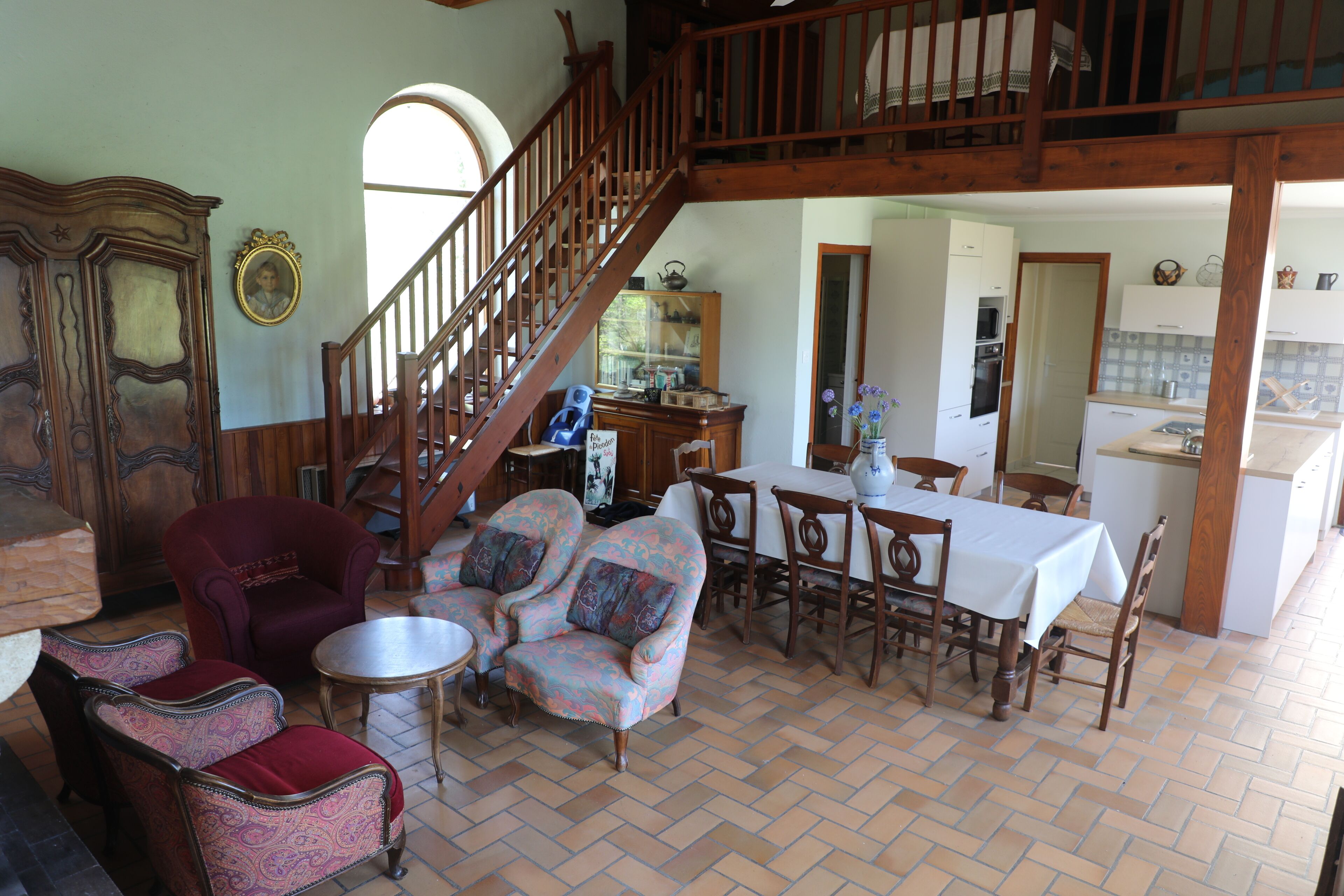 A spacious living area with a wooden staircase, a dining set, and a kitchen in the background.