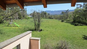 Un espacio al aire libre techado con vista a un campo verde y montañas a lo lejos.
