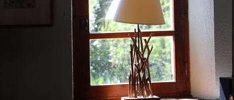 A room with a wooden-framed arched window, a lamp on a table, and a framed picture on the wall.