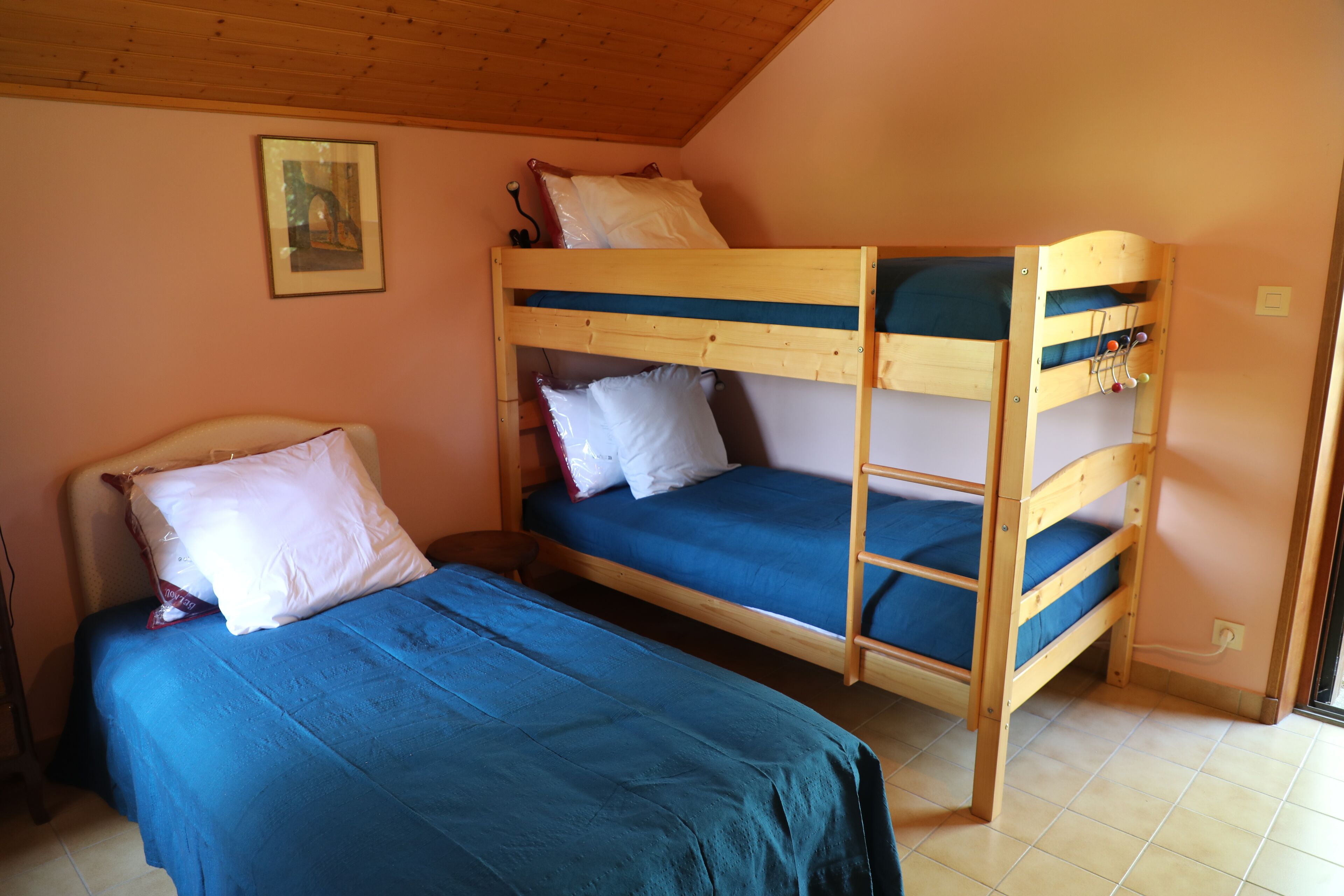 A room with two bunk beds, one with a lower bunk and one with a higher bunk. There is a single bed with a blue bedspread and a white pillow.