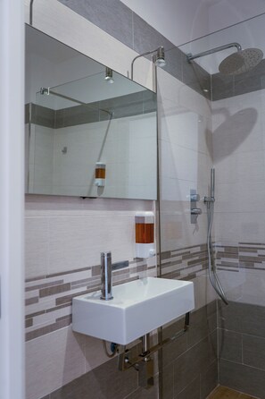 A modern bathroom with a glass-enclosed shower, a white sink, and a mirror. - NA Bella Vista Rooftop-B&B  (Naples)