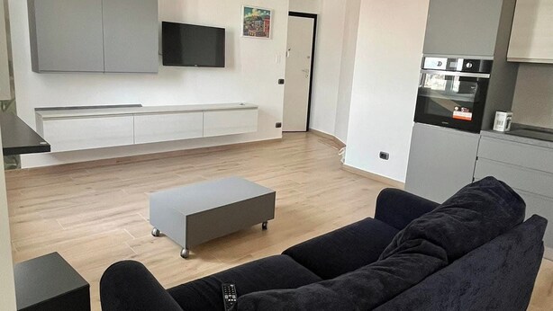 A modern living room with a black sofa, a small coffee table, and a TV mounted on the wall. - NA Bella Vista Rooftop-B&B  (Naples)