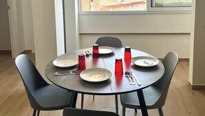 Een eetruimte met een ronde tafel voor vier personen, een raam met uitzicht op een stadsbeeld en een deur die naar een andere kamer leidt.