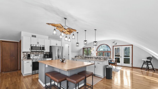 A spacious kitchen with a central island, wooden flooring, and pendant lighting. - Sunset Burrow Retreat in Roscommon, MI - whole house, 3 bed, 2.5 bath! (Roscommon)