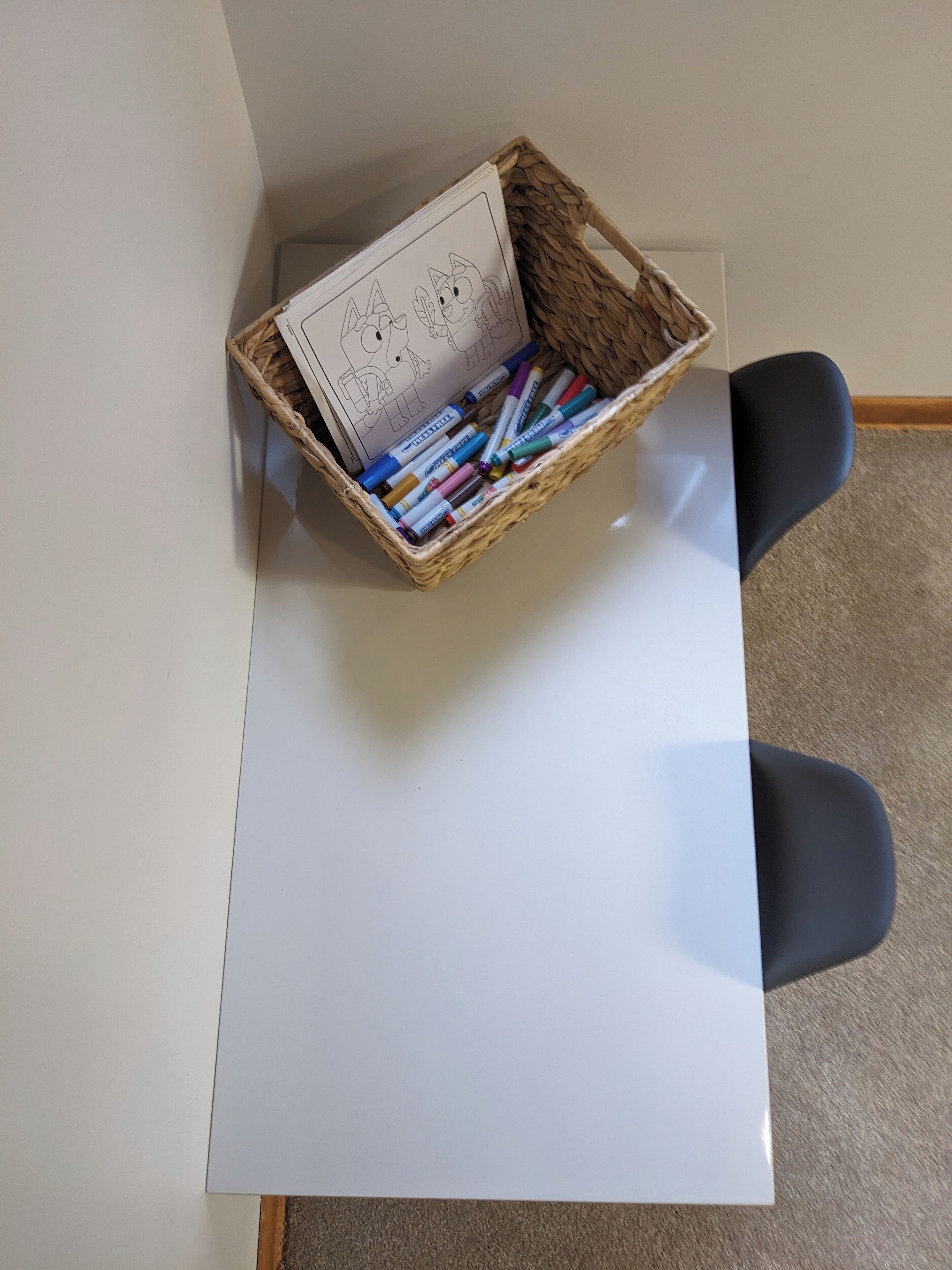A white desk with a wicker basket containing markers and a drawing pad.