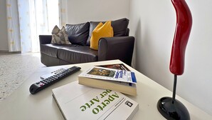 Una sala de estar con un sofá, almohadas, un control remoto, un libro y un objeto decorativo rojo.