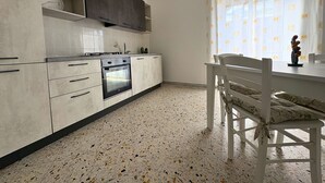 Una cocina con horno integrado, una mesa de comedor con sillas y una ventana con cortinas.