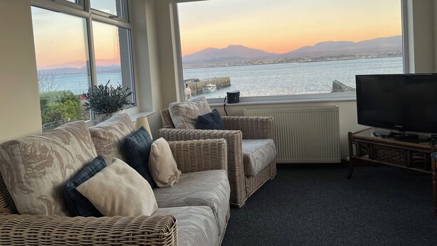 Una sala de estar con un juego de sofá, televisor y vistas a un cuerpo de agua y montañas.