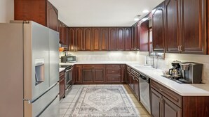 Une cuisine avec des meubles en bois, des appareils électroménagers en acier inoxydable et un tapis à motifs.