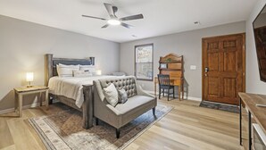 Une chambre à coucher avec un lit, un bureau, une chaise, une porte en bois et un ventilateur de plafond.
