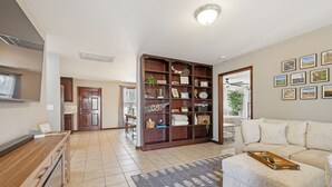 Un vaste espace de vie agrémenté d’une table basse en bois, d’un canapé beige et d’une grande bibliothèque remplie d’objets décoratifs.