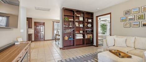 A spacious living area with a wooden coffee table, a beige sofa, and a large bookshelf filled with decorative items.