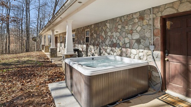Une façade en pierre, un bain à remous en bois, une véranda et une porte.