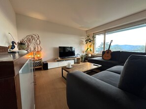 A modern living room with a sofa, a coffee table, a TV, and a guitar.