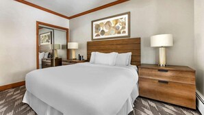 Une chambre d’hôtel avec un grand lit, une tête de lit en bois, deux tables de chevet avec des lampes, un miroir et une œuvre d’art abstraite encadrée accrochée au mur.