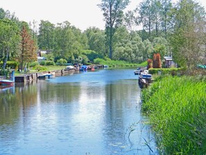 A calm river with boats docked on the left, surrounded by lush greenery and trees.