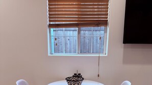 A room with a round white table, two white wicker chairs, a black and white woven basket, and a window with wooden blinds. - Comfort Studio Near 101/405 (Los Angeles)