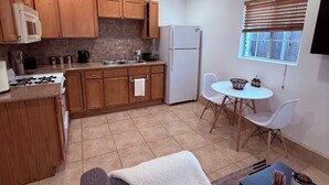 A compact kitchen with wooden cabinets, a white refrigerator, and a dining area with a white table and chairs. - Comfort Studio Near 101/405 (Los Angeles)
