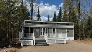 A two-story cabin with a front porch, surrounded by trees. - Cozy 1 1/2-bedroom, 4 Bed Tiny House with Gas Heat/AC, WiFi ATV/Snowmobile (Park Falls)