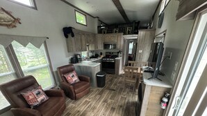 A spacious kitchen with wooden flooring, a dining area with two leather chairs, a built-in island, and a large window providing a view of the outdoors. - Cozy 1 1/2-bedroom, 4 Bed Tiny House with Gas Heat/AC, WiFi ATV/Snowmobile (Park Falls)