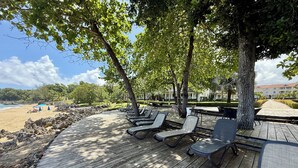 A wooden deck with lounge chairs, a beach view, and a building in the background. - Hispaniola Beach 2-Bdrm 1st floor Condo with Oceanview & Private Beach in Sosúa (Sosúa)