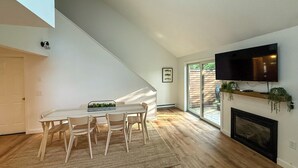 Een moderne woonkamer met een eethoek, een open haard en een aan de muur bevestigde televisie.
