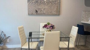 Un comedor con una mesa de vidrio, cuatro sillas blancas y un centro de mesa floral.