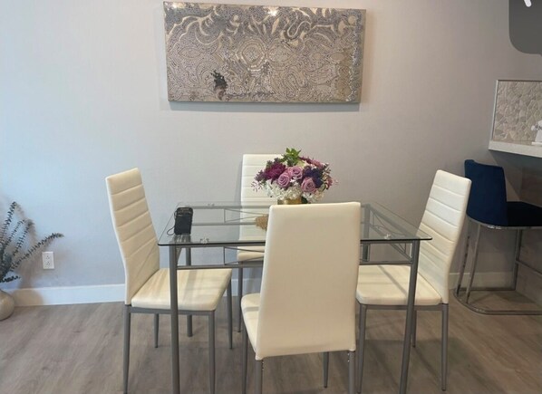 A dining area with a glass table, four white chairs, and a floral centerpiece.
