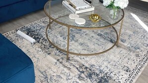 Una sala de estar con un sofá azul, una mesa de centro de vidrio y un jarrón blanco con flores.
