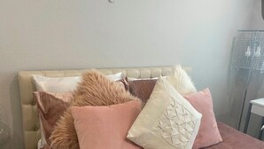 Una cama con cabecera capitonada, varios almohadones y una mesita de noche.
