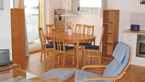 Ein gemütliches Wohnzimmer mit einem Holzesstisch, sechs Stühlen, einem Fernseher und einer Küchenzeile mit Herd und Schränken.