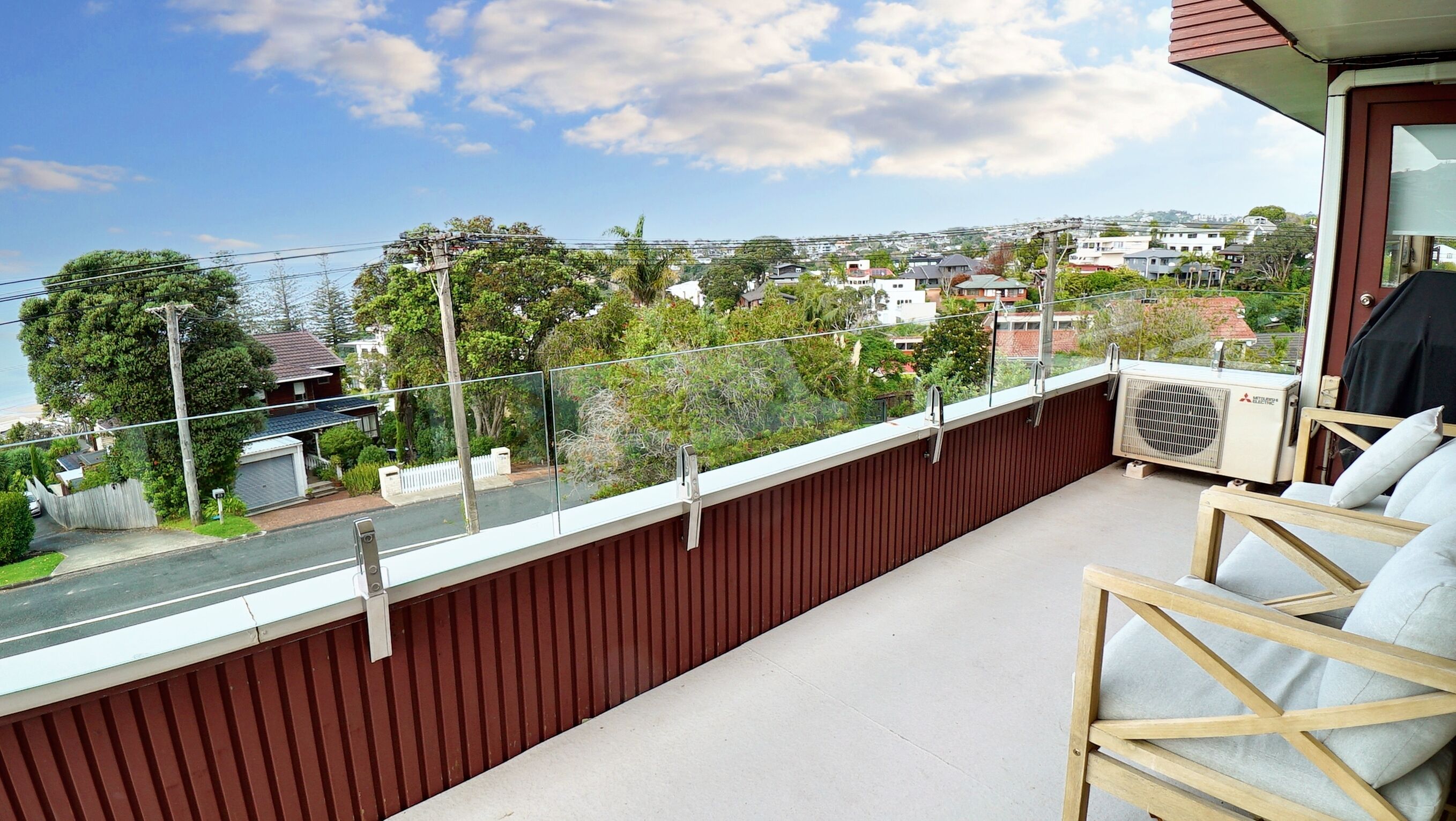 A balcony with a view of a residential area, a wooden fence, and an air conditioning unit.