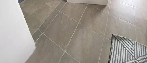 A room with a white door, grey walls, and tiled flooring.