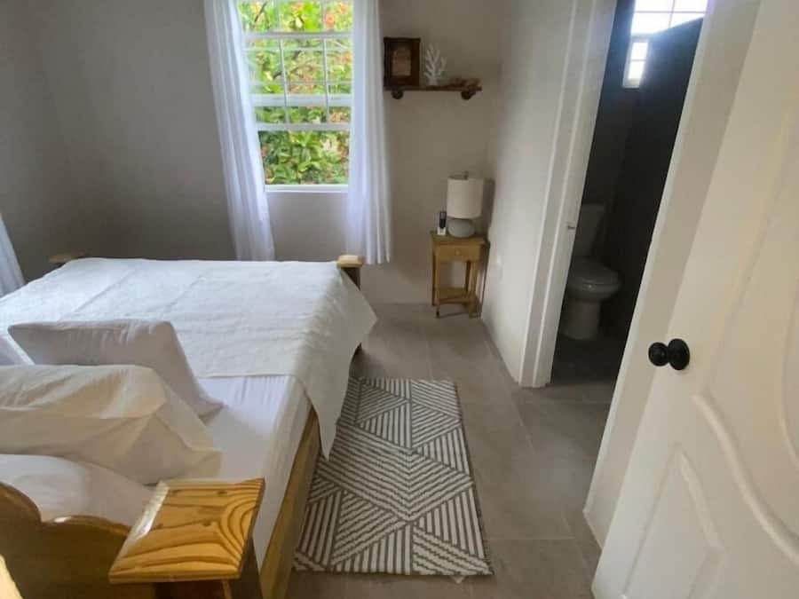 A bedroom with two beds, a small bedside table, a nightstand, a window with curtains, a door leading to a bathroom, and a geometric rug.