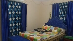 A bedroom with a bed, curtains, an air conditioner, and a nightstand. - Charming 1-bedroom house with AC, WiFi in peaceful St. Helena Village Piarco (St helena village piarco)