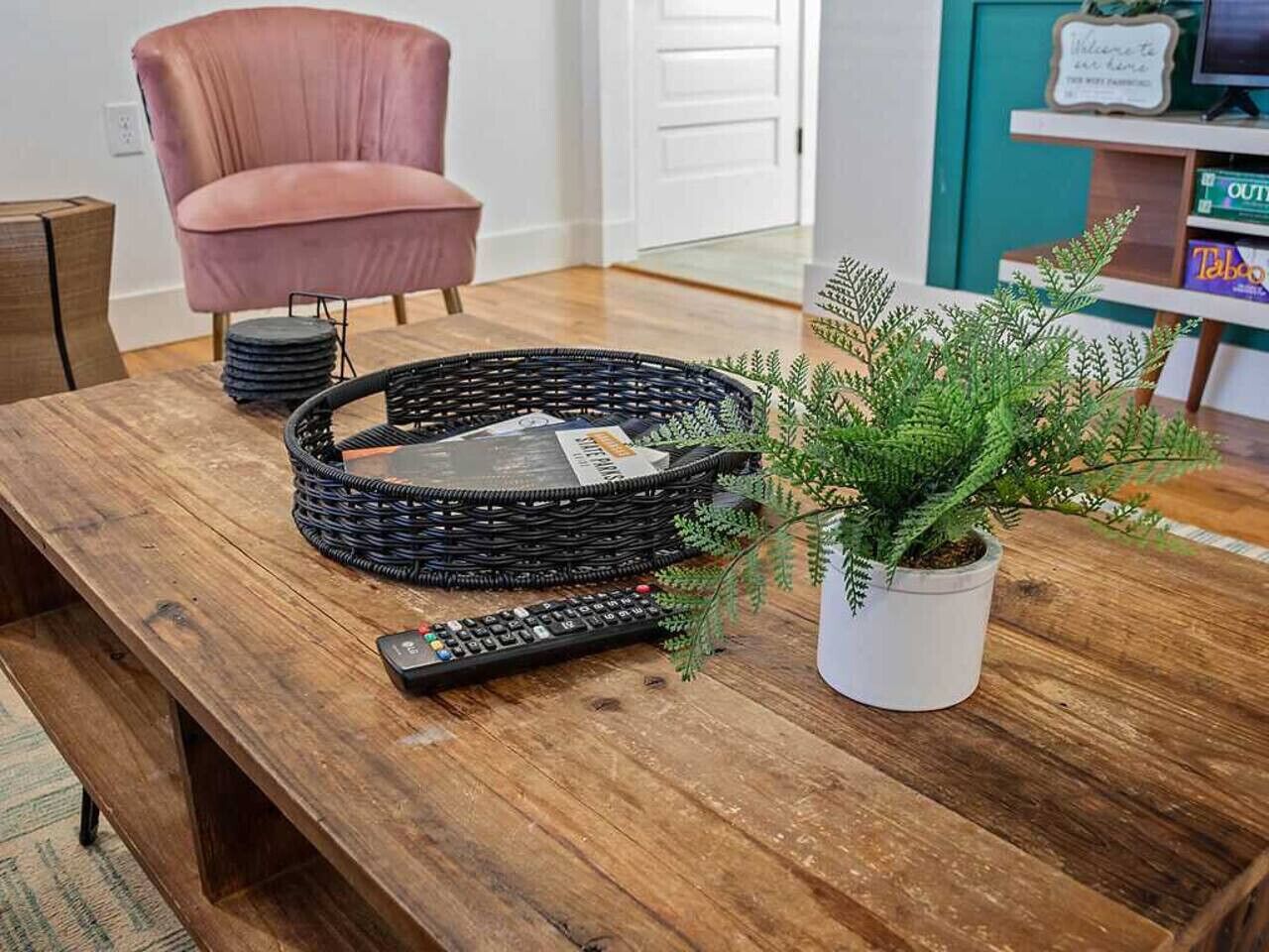 Una mesa de madera con una cesta tejida, un control remoto y una planta en maceta.