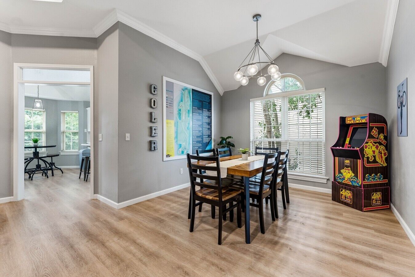 A dining area with a wooden table and chairs, a wall-mounted map, and a retro arcade machine.